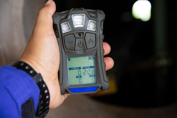 Human's hand holding the Portable Gas Detector for detect combustible gas , flammable gas , toxic gas and oxygen depletion in a confined spaces before starting work. - obrazy, fototapety, plakaty