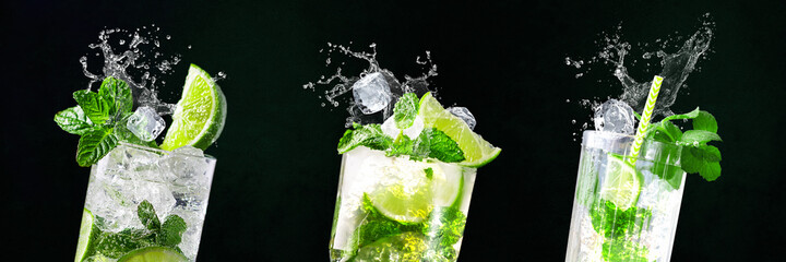 Glasses of Mojito with splashes and flying ice cubes on black and green background in bar | Limes,...