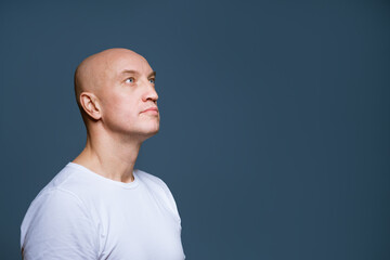 Bald man looking to the side on a blue background in a white t-shirt. Caucasian guy looks to the side with his head held high.