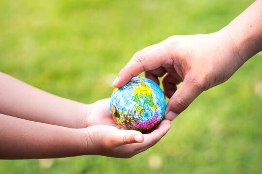 Joining forces to take care of global. Blurred green lawn background. Protect our globe. A mother's hands pass on a small world to her baby's little hands. To help protect and keep our planet livable.