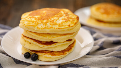 Stack of delicious pancakes sweet food with blueberries and blur dry leaves, plaid fabric in white plate on wooden background.