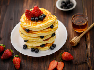 Sweet food. Stack of delicious pancakes with blueberries, Strawberry and honey in white plate on blur wooden background.