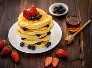 Sweet food. Stack of delicious pancakes with blueberries, Strawberry and honey in white plate on blur wooden background.