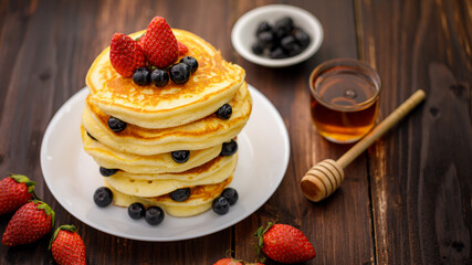 Sweet food. Stack of delicious pancakes with blueberries, Strawberry and honey in white plate on blur wooden background.