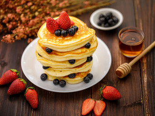 Sweet food. Stack of delicious pancakes with blueberries, Strawberry and honey in white plate on blur wooden background.