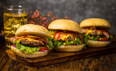 Selective focus on hamburgers with beef burgers, fried onions, spinach, ketchup and cheese. Served with beer.on wooden board loft background.