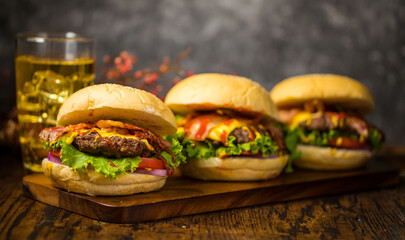 Selective focus on hamburgers with beef burgers, fried onions, spinach, ketchup and cheese. Served with beer.on wooden board loft background.
