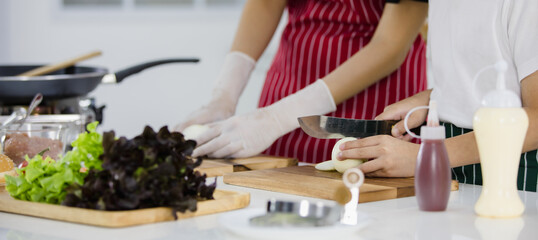 Unrecognized  boy cutting fresh onion near woman while cooking lunch together in contemporary light kitchen in weekend at home. Concept for education and learning by doing of modern kid