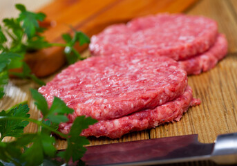 Shaped patties from raw ground meat and fresh greens on wooden background