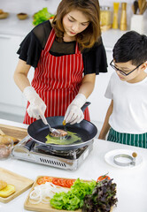 High angle of Asian boy making patties on hot pan near woman in apron while cooking burgers in kitchen together. Kid education and learning by doing concept