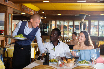 Fototapeta na wymiar Positive male waiter writing down order from visitors in restaurant