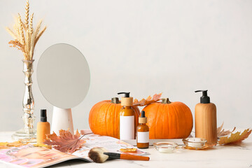 Pumpkins and bottles of cosmetic products on light background