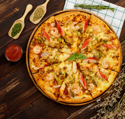 Banner of homemade seafood pizza with shrimp, crab sticks, bell peppers topping on wooden tray, table, decorated by tomato sauce, ketchup, oregano ingredients with napkin in kitchen and copy space.