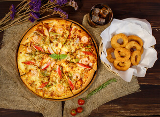 Vertical photo and close up on tasty homemade seafood pizza on sackcloth with dried flowers, cold beverage, Fried onions on wooden table. Food and Beverage Concept.