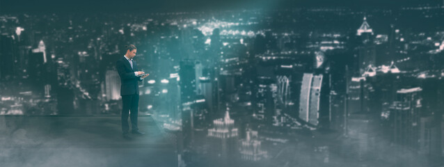 Businessman using tablet,standing on building  rooftop to looking cityscape at night,concept...
