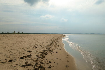 The coastal line of a sandy beach by the Baltic Sea on Sobieszewo island, Poland. The sea is gently waving. A bit of overcast. Solitude and serenity
