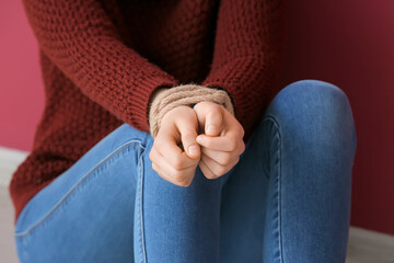 Female hostage with tied hands sitting on floor in room, closeup