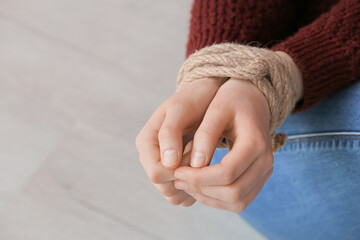 Female hostage with tied hands sitting on floor in room, closeup