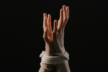 Female hostage with tied hands on dark background, closeup