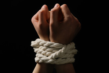 Female hostage with tied hands on dark background, closeup