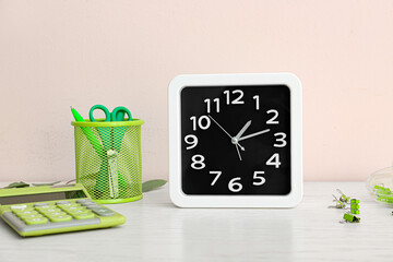 Stylish clock and stationery on table near light wall