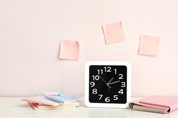 Fototapeta na wymiar Stylish clock with notebooks on table near light wall