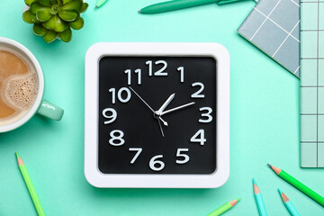 Stylish clock with stationery and cup of coffee on color background