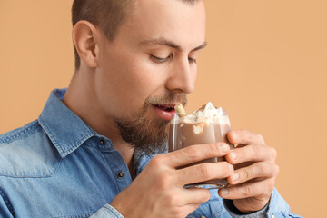 Handsome man drinking hot cocoa on color background