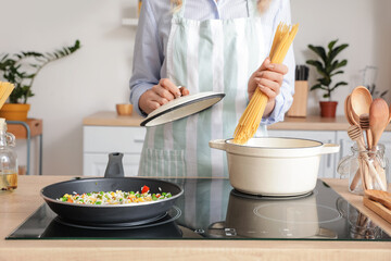 Woman cooking tasty pasta on kitchen stove, closeup
