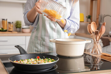 Woman cooking tasty pasta on kitchen stove, closeup