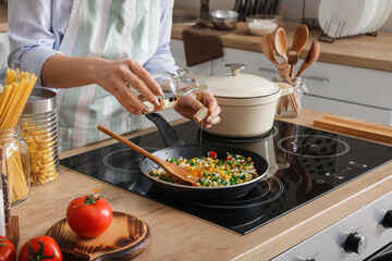 Woman cooking tasty rice with vegetables on stove in kitchen, closeup - Powered by Adobe