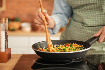 Woman cooking tasty rice with vegetables on stove in kitchen, closeup