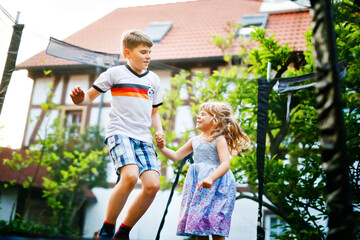 Fototapeta premium Little preschool girl and school kid boy jumping on trampoline. Happy funny siblings children having fun with outdoor activity in summer. Sports and exercises for kids. Family have fun.