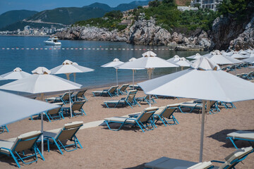 Empty white sun loungers without people under umbrellason the pebble beach by the sea.