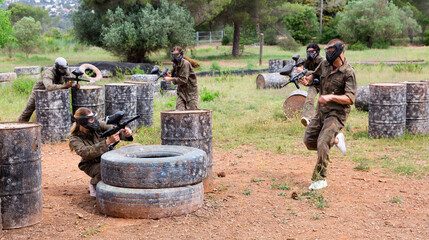 Fototapeta premium Dynamic paintball battle, players jumping and aiming with guns outdoors