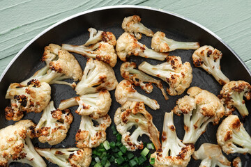 Frying pan with tasty fried cauliflower on color wooden background, closeup