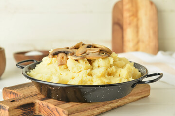 Frying pan with tasty mashed potatoes and mushrooms on light wooden background