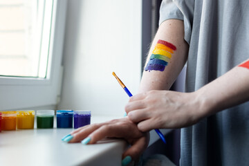 an artist girl with a rainbow painted on her arm stands at the window