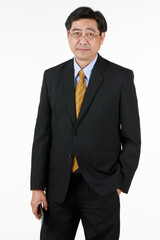 One old businessman in formal black suit yellow tie. Standing look at camera one hand put in pant pocket other hand holding mobile phone. Studio shoot with white background.