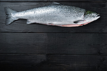 Fresh raw trout red fish on black wooden surface, top view with copy space