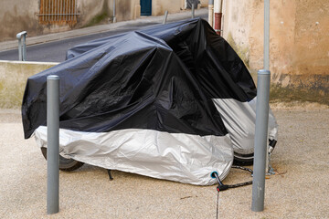 two motorcycles protected by black grey protective under cover black grey silver in city street motorbike with tarpaulin jacket