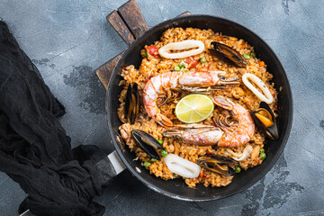 Paella with seafood, prawns, musselsm chicken and rice in pan on grey background, top view