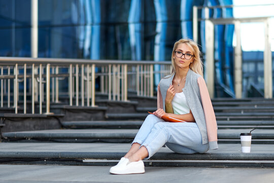 Portrait of an attractive happy woman holding coffee cup while sitting on stairs at the city street