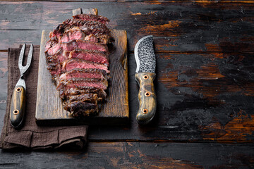 Rare rib eye steaks with herbs and spices, on wooden serving board, with meat knife and fork, on...