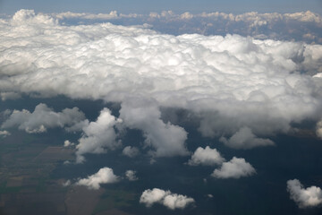 Aerial view from airplane window of white puffy clouds on bright sunny day.