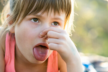 Beautiful child girl pinching nose and showing tongue.
