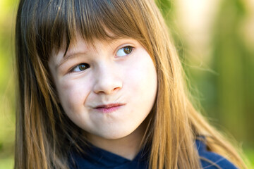 Close up portrait of pensive cute brunette child girl in park.