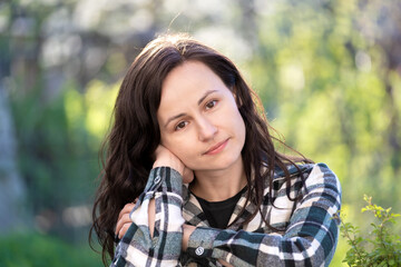 Portrait of thoughtful pretty young woman relaxing outdoors on warm spring sunny day.