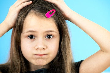 Close up portrait of upset and pensive little girl with cute pink hairpin on blue background.