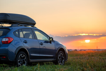 SUV car with roof rack luggage container for off road travelling parked at roadside at sunset. Road trip and getaway concept. - obrazy, fototapety, plakaty